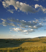 Light clouds in a wide blue sky over rolling grasslands.