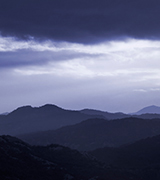 Misty hills beneath dark clouds at dusk.